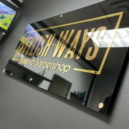 "Stylish Ways Salon & Barbershop" business sign with gold lettering on a glossy black background, mounted on a gray wall. The sign features a sleek and modern design, reflecting the upscale ambiance of the establishment.