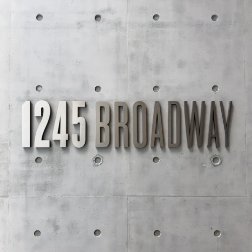 Exterior business signage displaying the address name in bold, metallic letters mounted on a concrete wall. The sign uses a modern, sans-serif font and the clean, minimalist design complements the industrial-style surface.