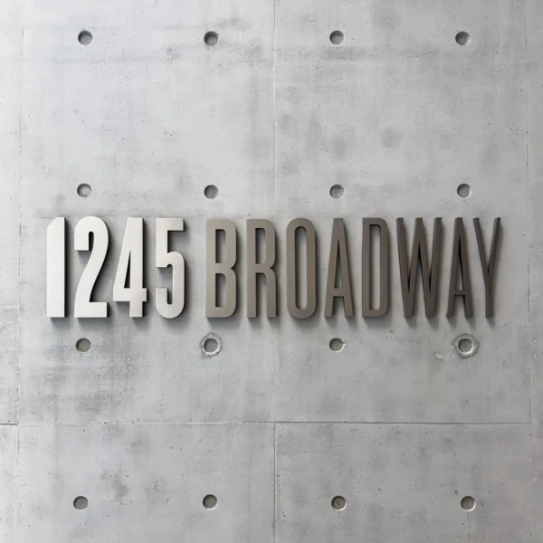 Exterior business signage displaying the address name in bold, metallic letters mounted on a concrete wall. The sign uses a modern, sans-serif font and the clean, minimalist design complements the industrial-style surface.