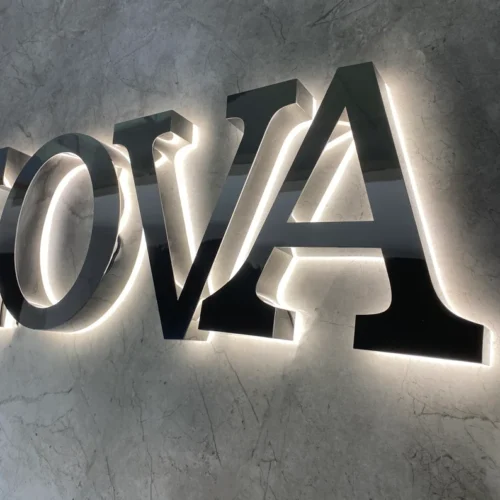 Illuminated black metal signage letters mounted on a marble wall, featuring the letters. The sign has a sleek and modern design, with a subtle backlit glow enhancing visibility and adding an elegant touch. Ideal for business or event signage.