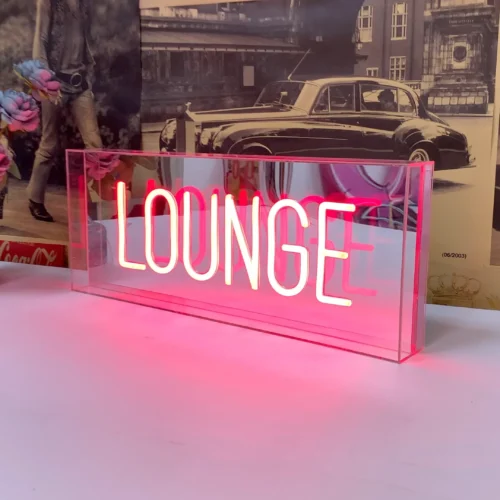 Neon sign with the word "LOUNGE" in pink letters, encased in a clear acrylic box, positioned on a table.