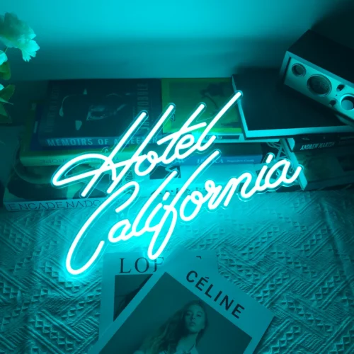 Neon sign with the words "Hotel California" in cursive, glowing in blue, placed on a table with books and magazines. The sign creates a retro and nostalgic ambiance, reminiscent of the famous song.