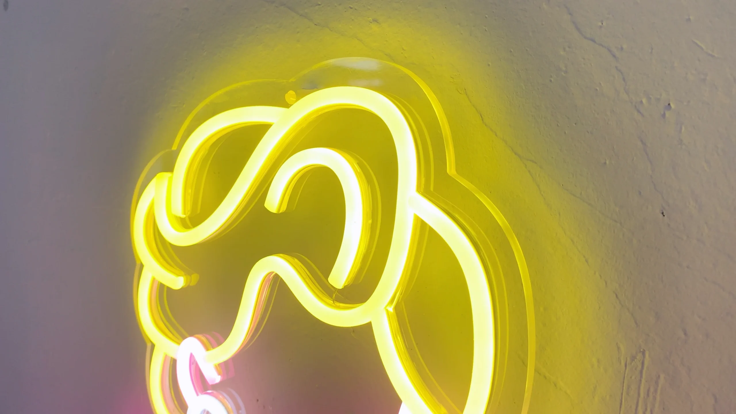 Neon sign depicting a stylized figure of Marilyn Monroe in her iconic pose with a flowing dress. The sign features bright colors, with yellow for her hair, pink for her dress and body, and white for the dress details and shoes.