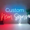 Neon sign displaying the words "Custom Neon Signs" mounted on a plain wall. The word "Custom" is in blue, "Neon" in red, and "Signs" in white.