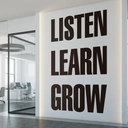 Wall signage in a modern office reading "LISTEN LEARN GROW" in bold, black letters. The motivational message is displayed on a white wall with subtle backlighting, enhancing the clean, professional aesthetic of the workspace. Ideal for promoting a positive and productive work environment.