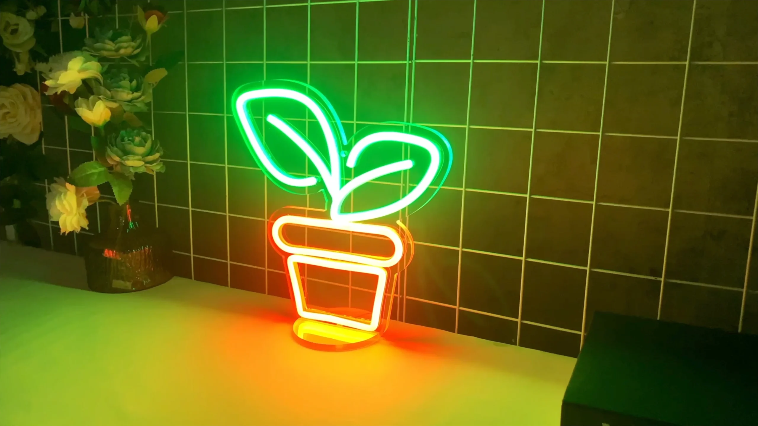 A desktop neon sign depicts a green-leaf plant and an orange flowerpot. The sign is placed on a desk, emitting vibrant light, and can be dimmed. It can also serve as a night light and an ambient light.