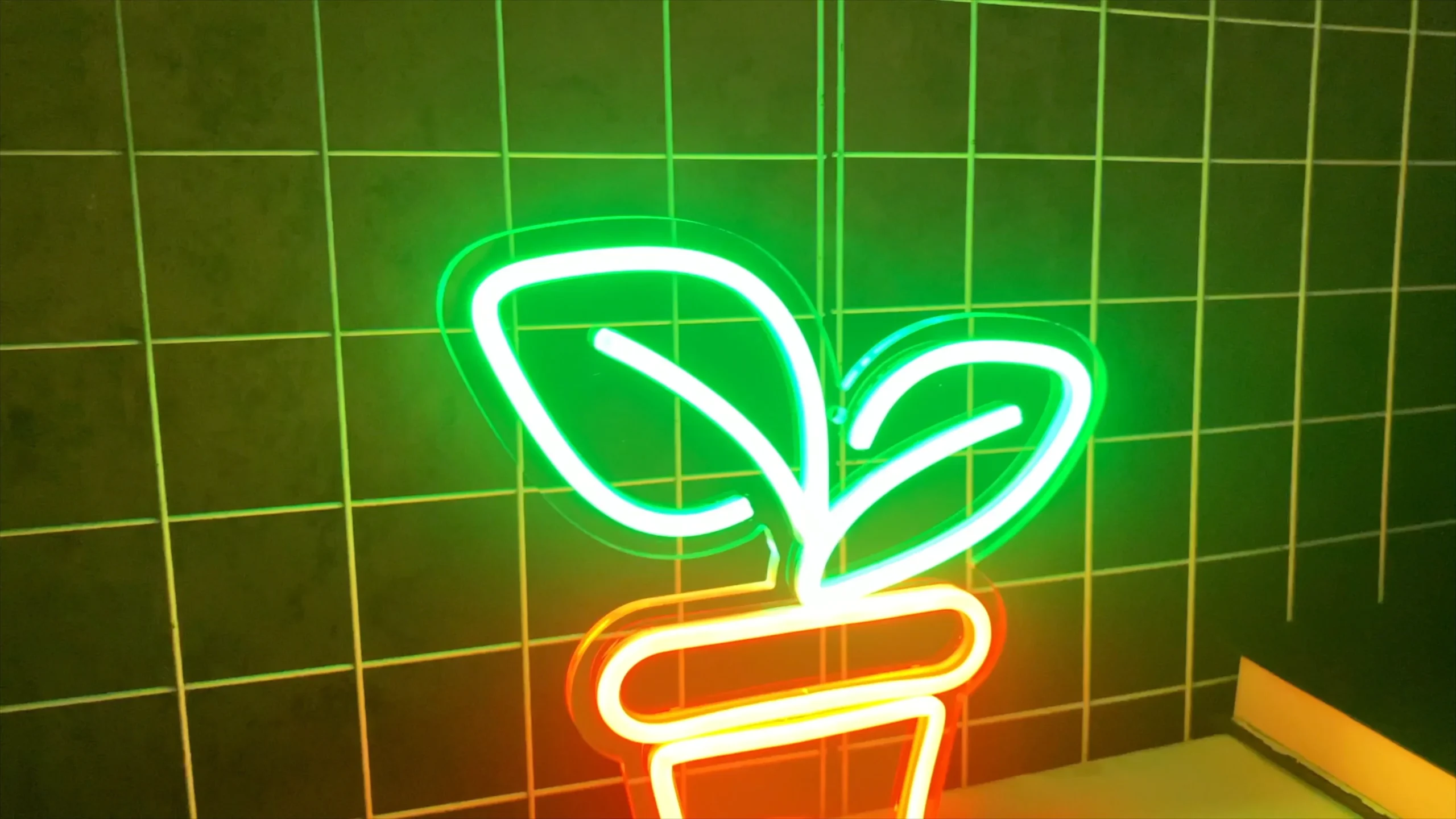 A desktop neon sign depicts a green-leaf plant and an orange flowerpot. The sign is placed on a desk, emitting vibrant light, and can be dimmed. It can also serve as a night light and an ambient light.