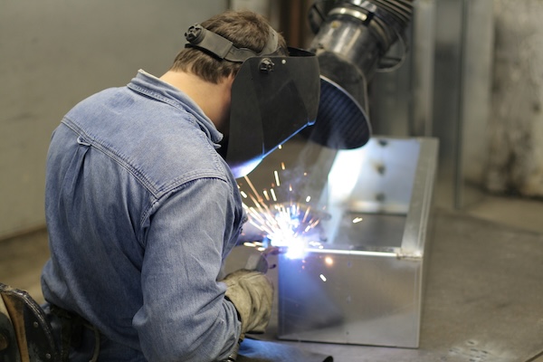 A worker wearing a protective mask and gloves welding a metal frame for a business sign. 