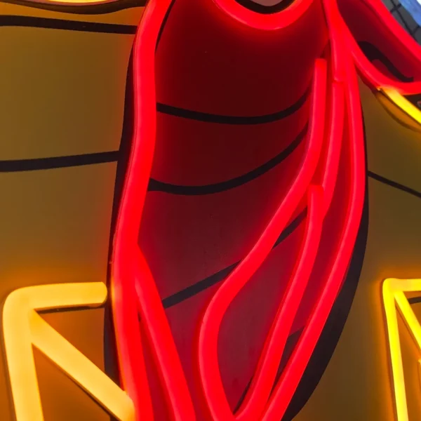 Close-up of a neon sign showing detailed red and yellow neon tubing forming part of a cowboy's bandana.