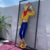 Neon sign of a cowboy waving, brightly colored in yellow, red, and blue, placed against an outdoor white wall with a palm plant nearby.