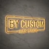 Backlit sign "BY CUSTOM HAIR STUDIO" in a metallic frame on a marble-patterned wall.