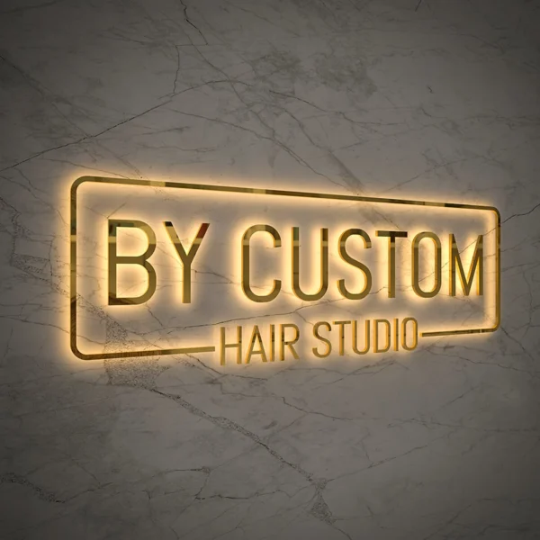 Backlit sign "BY CUSTOM HAIR STUDIO" in a metallic frame on a marble-patterned wall.