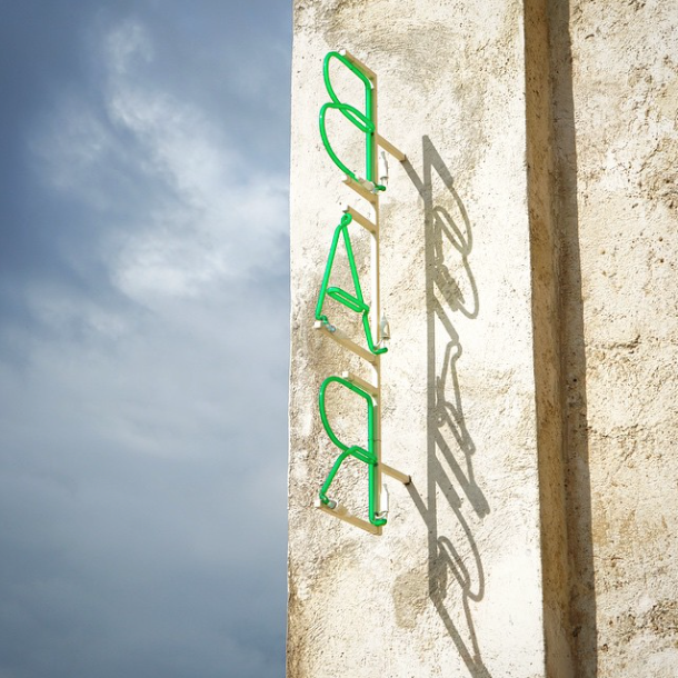 A vertical green neon "BAR" sign mounted on the exterior wall of a building. The sign consists of green neon tubing spelling the word "BAR" in a vertical stack.