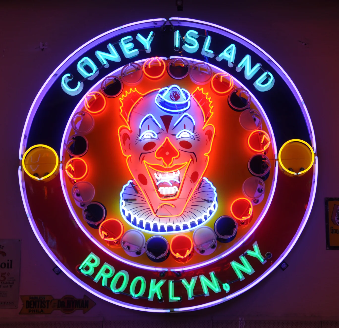 Neon sign depicting a vibrant clown face with "Coney Island" written above and "Brooklyn, NY" below. The sign is circular with neon lights in red, blue, and green.